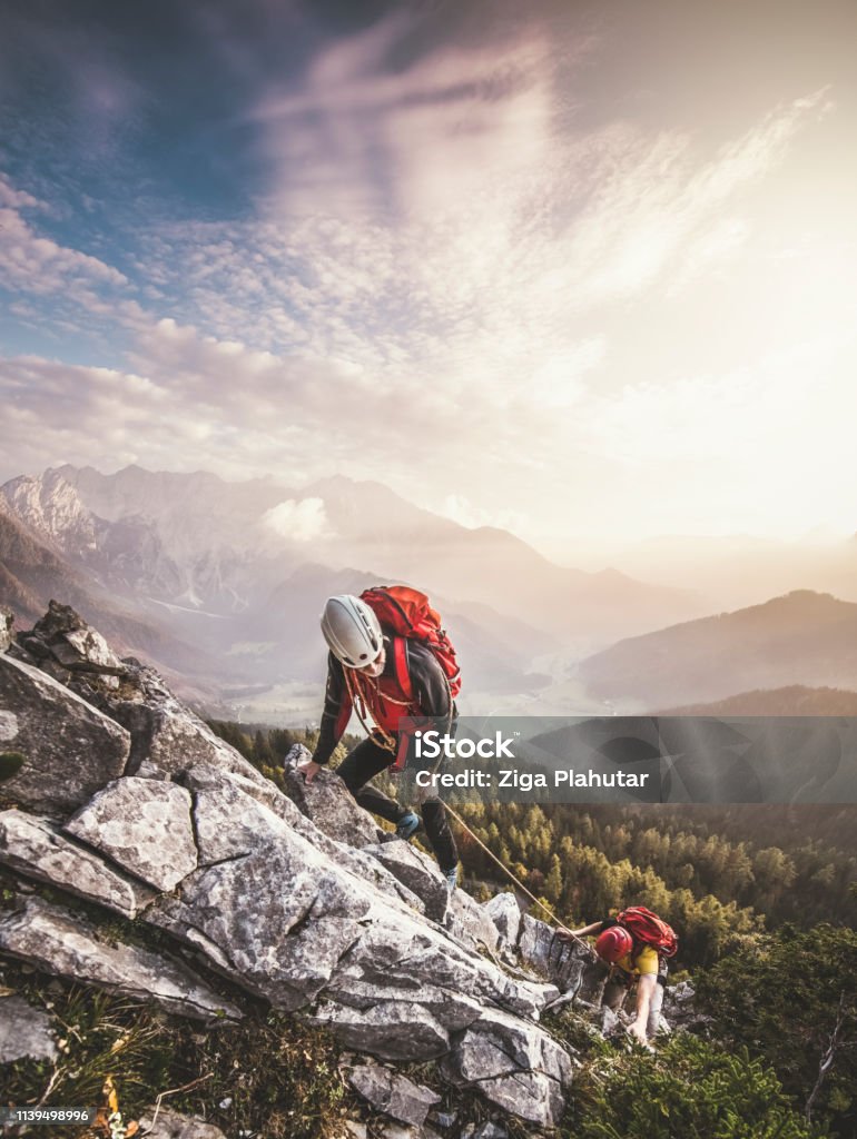 Couple of mountain climbers, climbing via ferrata, a secure climbing route Couple climbing via ferrata, a secure climbing route found in Alps. Alpine climbing on a sunny day in the mountains. Valley covered in fog, temperature inversion in the valley. Mountain Climbing Stock Photo