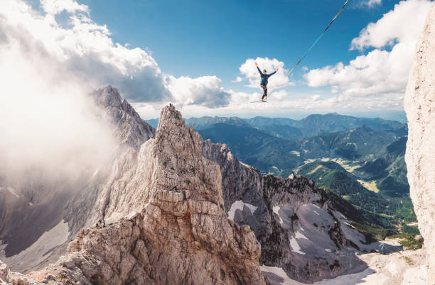 Bold move - Slack line Man walking on slack line in the mountains, high up in the air on a beautiful sunny day. Dangerous sports. highlining stock pictures, royalty-free photos & images