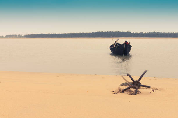 Boat and river at Tajpur, West Bengal, India Moody image of a boat on water tied by a rope with an anchor on river bed at Tajpur, West Bengal, India. Minimalistic image. bay of bengal stock pictures, royalty-free photos & images