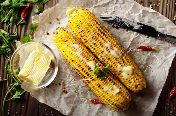 vista superior da tabela da cozinha com a espiga de milho doce grelhada a manteiga e os verdes de derretimento no papel de cozimento - corn corn on the cob grilled roasted - fotografias e filmes do acervo