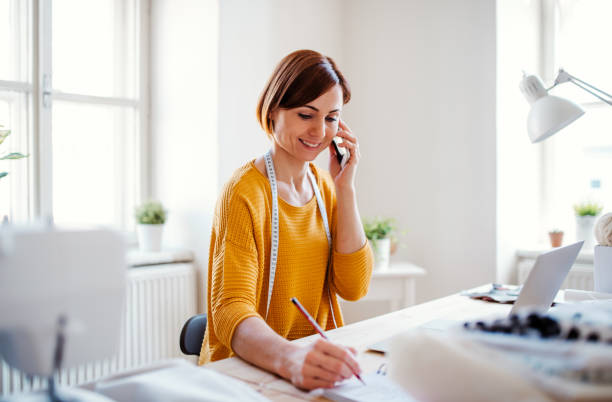 istock Young creative woman in a studio, using smartphone. A startup of tailoring business. 1139516014
