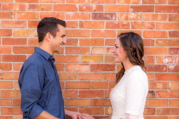 Photo of Attractive Young Couple Holding Hands and Staring at Each Other in Front of a Brick Wall