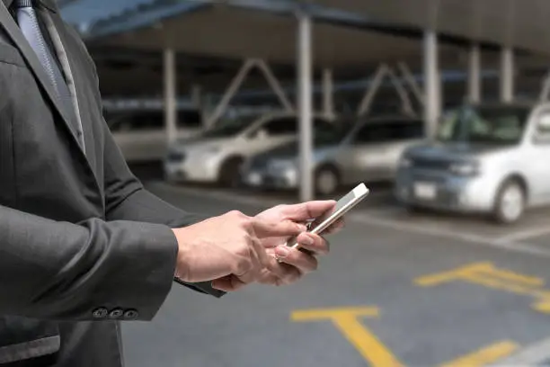 Car sharing service or rental concept. Sharing economy and collaborative consumption. Customer man suit hand using smart phone with blur cars background with fare light effect.