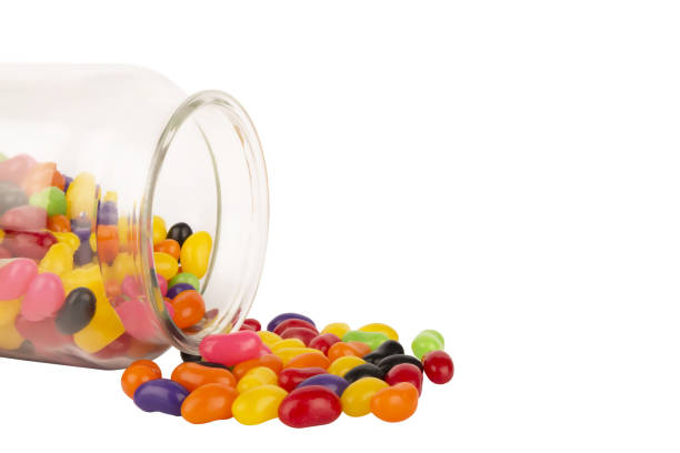istock Small glass jar with colored jelly beans scattered isolated on white background. 1139529140