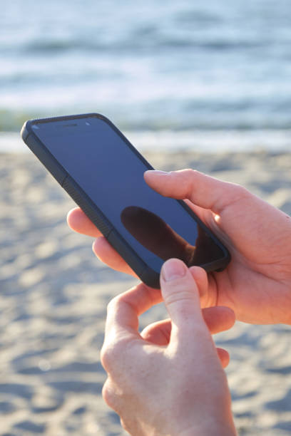 istock Mockup image of a woman's hands holding a mobile phone on the beach. Selective focus 1139529337