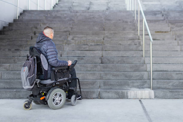 Man on a wheelchair looking at stairs Disabled man with muscular dystrophy on an electric wheelchair who can't get up the stairs. Accessibility concept. atrophy photos stock pictures, royalty-free photos & images