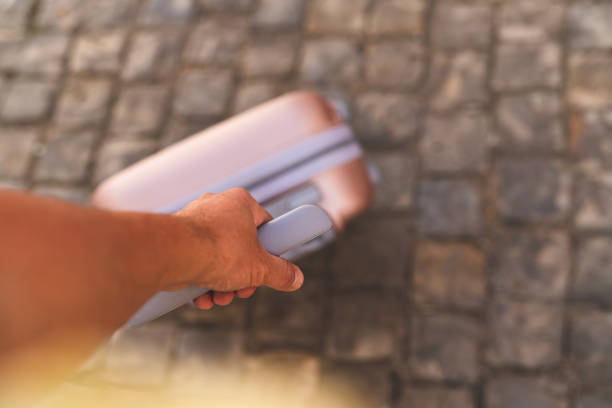 A man is carrying a modern pink suitcase through a European city on summer vacation.