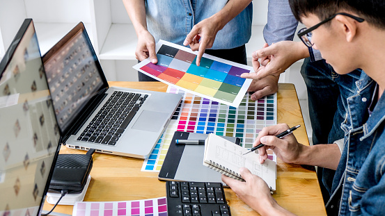 Team of young colleagues creative graphic designer working on color selection and drawing on graphics tablet at workplace, Color swatch samples chart for selection coloring.