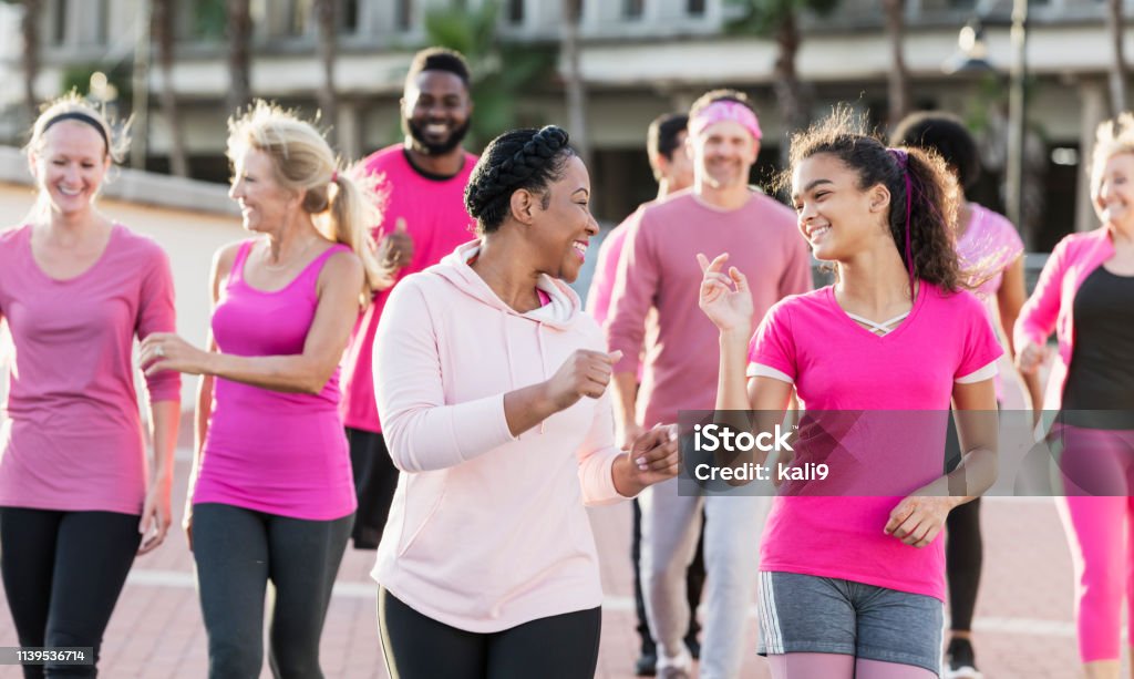Group of women and men in pink, at breast cancer rally A multi-ethnic group of nine women and men of mixed ages walking together outdoors, wearing pink, at a breast cancer awareness rally, raising money to find a cure. The focus is on the mid adult African-American woman in the foreground and the mixed race girl walking beside her. She is in her 30s and her teenage friend is 13 years old. Walking Stock Photo