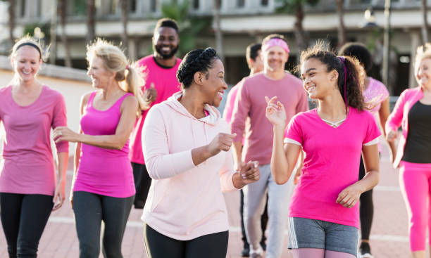 Group of women and men in pink, at breast cancer rally A multi-ethnic group of nine women and men of mixed ages walking together outdoors, wearing pink, at a breast cancer awareness rally, raising money to find a cure. The focus is on the mid adult African-American woman in the foreground and the mixed race girl walking beside her. She is in her 30s and her teenage friend is 13 years old. charity benefit photos stock pictures, royalty-free photos & images