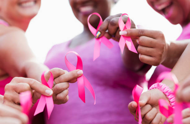 Group of women in pink, breast cancer awareness ribbons Cropped view of a multi-ethnic group of women of mixed ages standing together outdoors, wearing pink, at a breast cancer awareness rally, raising money to find a cure. They are each holding a breast cancer awareness ribbon. The focus is on their hands. breast cancer stock pictures, royalty-free photos & images
