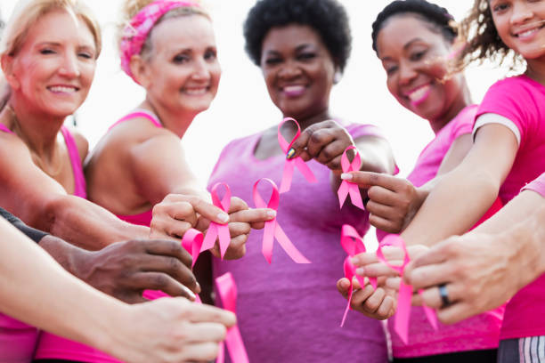Group of women in pink, breast cancer awareness ribbons A multi-ethnic group of five women of mixed ages standing together outdoors, wearing pink, at a breast cancer awareness rally, raising money to find a cure. They are each holding a breast cancer awareness ribbon. The focus is on their hands. breast cancer stock pictures, royalty-free photos & images
