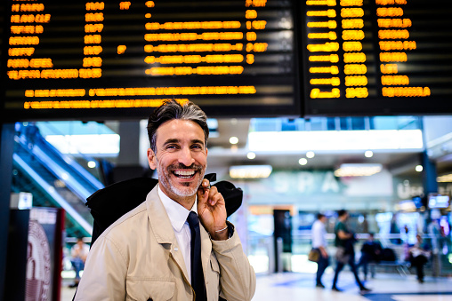 Smiling elegant man at the airport waiting for a flight. He is holding a luggage