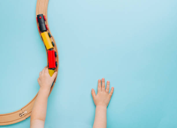 Kids hands playing with wooden toy train on blue background Kids hands playing with wooden toy train on blue background with blank space for text. Top view, flat lay. miniature train stock pictures, royalty-free photos & images