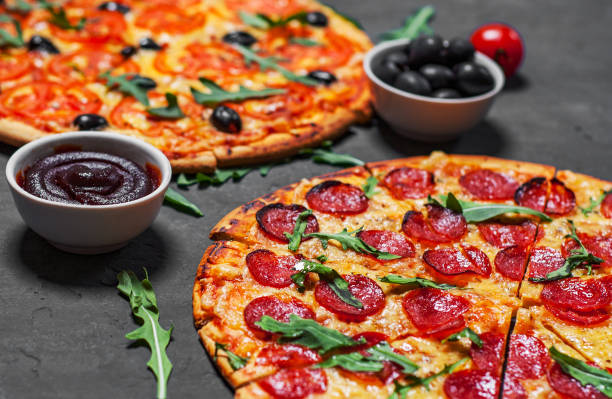 istock Pepperoni Pizza and Pizza with Mozzarella cheese, Tomatoes, pepper, olive, Spices and Fresh arugula. Pizza Margherita or Margarita on Dark grey black slate background 1139545292
