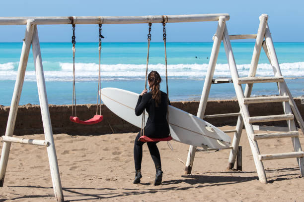 istock Woman with surfboard sitting on swing 1139553756