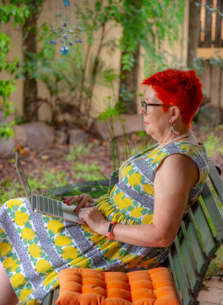 рыжеволосая женщина в очках наслаждается использованием ноутбука в своем саду. - 5440 стоковые фото и изображения