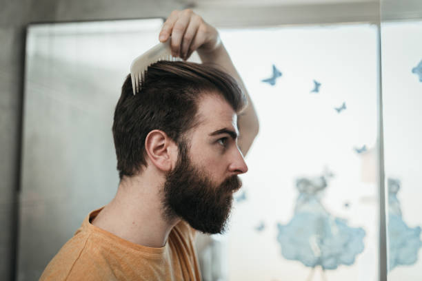 el hombre joven peinando el cabello en el baño - peine fotografías e imágenes de stock