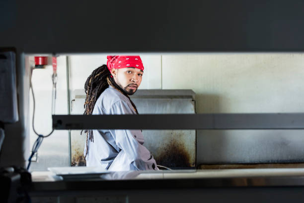 A young mixed race African-American, Hispanic and Native American man in his 20s working as a chef in a restaurant, in the kitchen. He is wearing a do rag, apron and gloves.