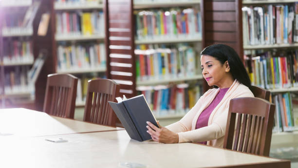 istock Mature Hispanic woman reading book in library 1139566090