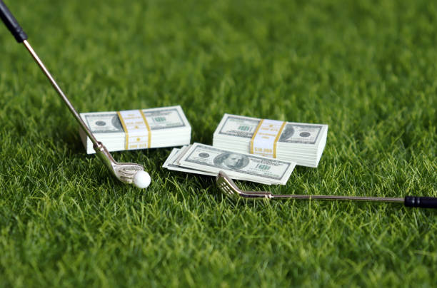 istock A bundle of bills and golf equipment on the green grass. 1139566267