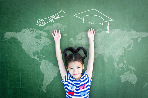 Scholarship opportunity and education success concept with school kid with doodle drawing of graduation cap on green chalkboard