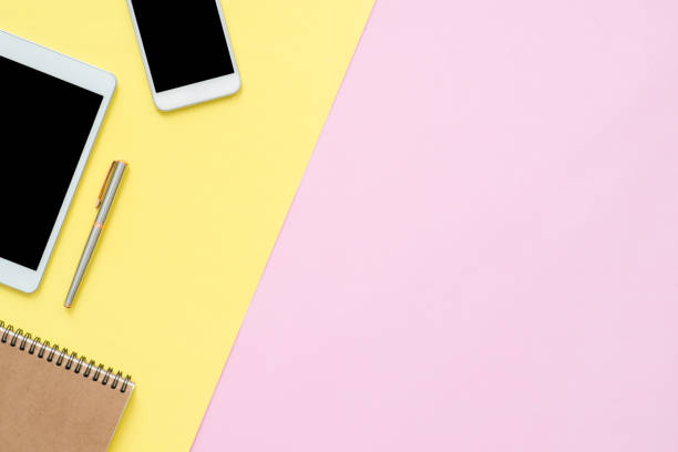 istock Office desk working space - Flat lay top view of working space with blank notebook page and blank empty mock up phone tablet on pastel background. Pastel pink yellow color background space concept. 1139567168