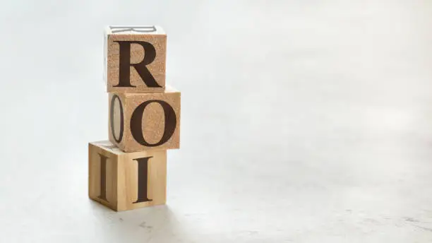 Photo of Pile with three wooden cubes - letters ROI meaning Return on Investment on them, space for more text / images at right side.