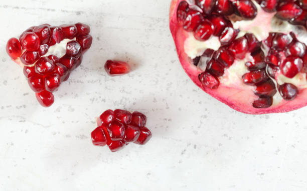 istock Pomegranate halved, gem like fruits next to it on white stone board, top down view. 1139567596