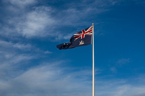 Waving Australian national flag against blue sky on the background.