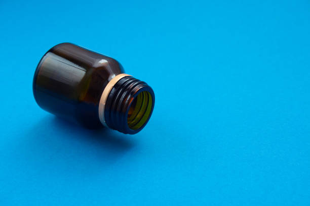 Empty glass dark bottle without pills on blue background. Medicines deficit concept. Copyspace
