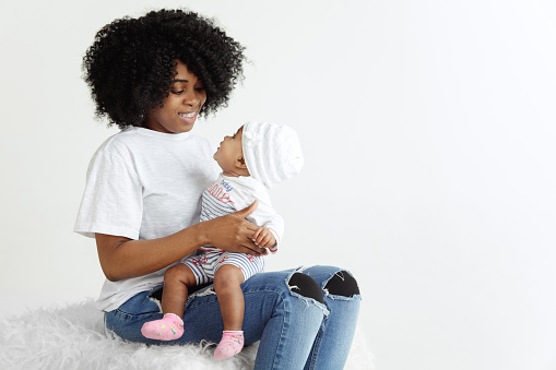 Closeup portrait of beautiful african woman holding on hands her little daughter on white background. Family, love, lifestyle, motherhood and tender moments concepts. Mother's day concept or background