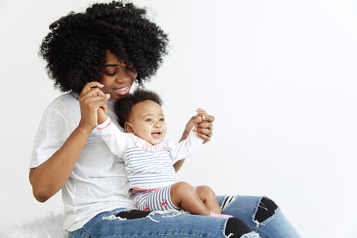 Closeup portrait of beautiful african woman holding on hands her little daughter on white background. Family, love, lifestyle, motherhood and tender moments concepts. Mother's day concept or background