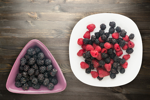blackberries and raspberries on a plate. blackberries and raspberries on wooden background. vegetarian food .