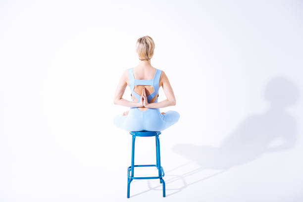 Yoga and asana. Beautiful blonde woman holding hands behind her while sitting on the stool