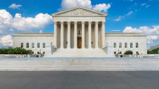 The United States Supreme Court Building and American flag at sunny day in Washington DC, USA.