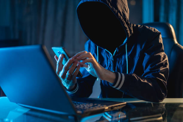 Anonymous hacker programmer uses a laptop to hack the system in the dark. Concept of cybercrime and hacking database stock photo
