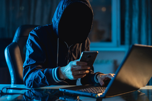 Programador de hackers anónimo utiliza un ordenador portátil para hackear el sistema en la oscuridad. Concepto de ciberdelincuencia y base de datos de piratería photo