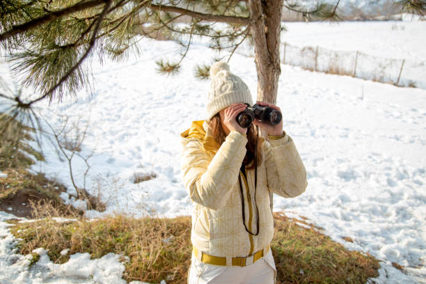 istock The girl in a White cap with a backpack in the winter in a forest looking through binoculars 1139602840