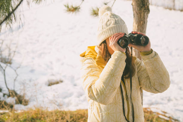 istock The girl in a White cap with a backpack in the winter in a forest looking through binoculars 1139602849