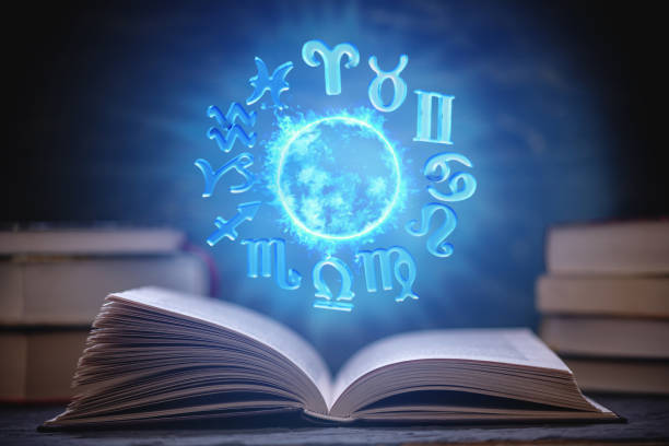 Open book on astrology on a dark background. The glowing magical globe with signs of the zodiac in the blue light stock photo