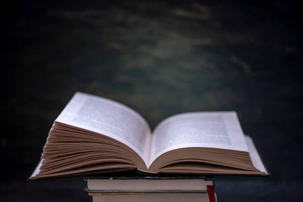 istock Open book on a stack of books on a table on a dark background. Education and reading of paper books 1139603549