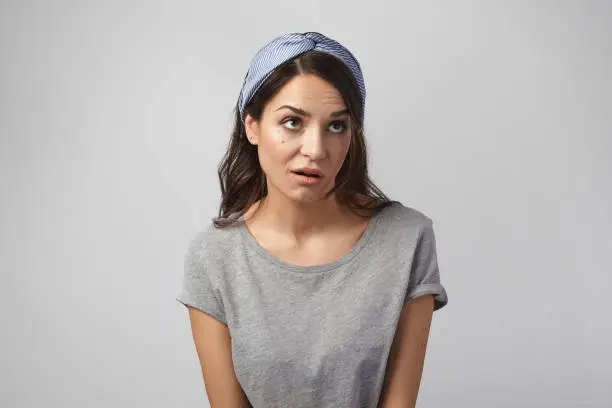 Funny emotional young Caucasian woman wearing gray top and headscarf grimacing, rolling her eyes, expressing annoyance, pissed off or bored with something. Human emotions, reaction and attitude