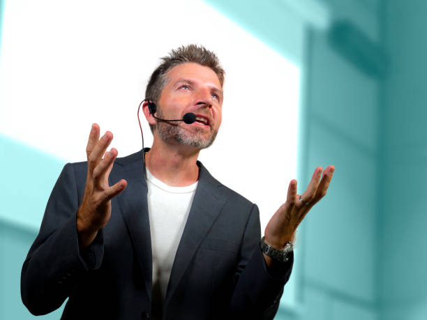 young attractive and confident successful man with headset speaking at corporate business coaching and training auditorium conference room talking giving motivation training from speaker stage stock photo