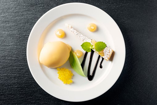 Overhead view of a lemon themed dessert. Consisting of a lemon tart, lemon shaped and coloured chocolate lemon with concentrated lemon pearls and lemon infused apple balls. Colour, horizontal with some copy space.