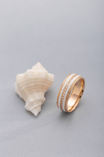 istock Gold ring with white enamel and diamonds on gray background with seashell 1139612544