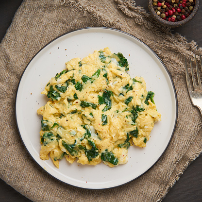 Pan-fried scrambled eggs and spinach, cup of tea on dark brown background. Breakfast with omelette, top view