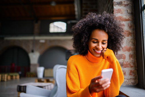 Smiling African American woman using mobile phone while drinking coffee.