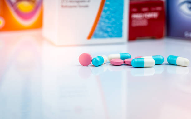 Round pink tablets pill and white-blue capsule pills on blurred background of drug packaging. Painkiller medicine. Drug use for treatment migraine headache. Pharmacy product. Pharmaceutical industry. pastilla de comprimidos rosados redondos y píldoras de cápsulas de color blanco-azul sobre fondo borroso de envases de fármacos. medicina del analgésico. uso de drogas para el tratamiento de cefalea migraña. producto de farmacia. industria farmacéuti