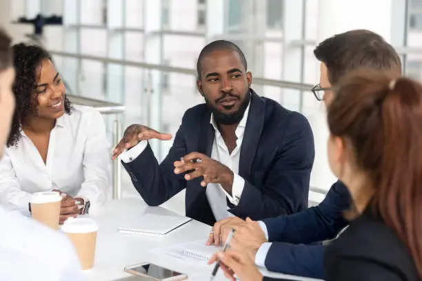 Photo of Black millennial boss leading corporate team during briefing in boardroom